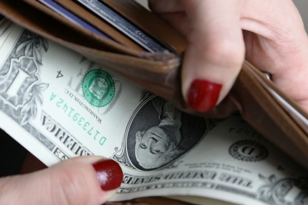 an open wallet held by a woman's hand with painted fingernails. Wallet shows US dollars inside